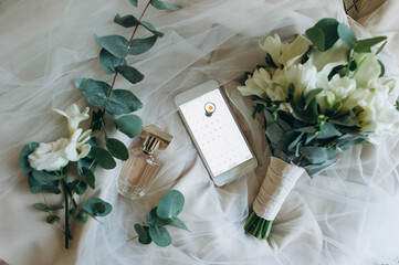 Bride's bouquet, perfume and a ring on the phone that marks the wedding date lie on the veil.