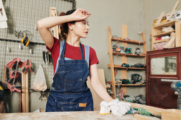 Young female carpenter wiping sweat after working with wood in carpentry shop