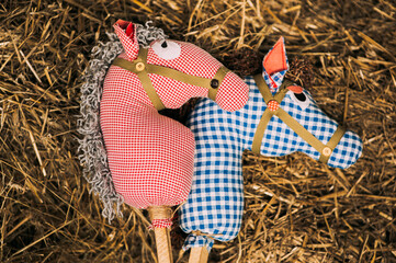 Two retro cotton fabric horse toy on a stick lying on the hay. Vintage rustic background.