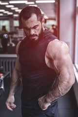 strong young bearded caucasian male athlete with big muscles wearing black sportswear in sport fitness gym