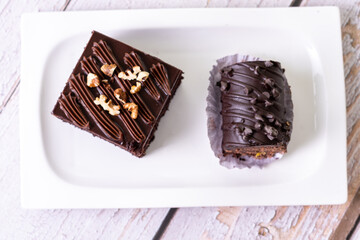 chocolate cakes pastries brownies on white ceramic plate with nuts topping  on a white wooden rustic desk table