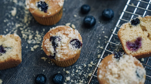 Blueberry muffin topped with crumble on a dark textured background and cooling rack
