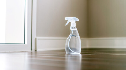 Spray bottle in a side view with a clear liquid inside on the wooden floor in an empty space at...