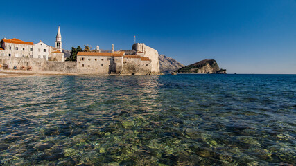 Fototapeta na wymiar Strand mit himmel und Stadtmauer mit Burg und hafen von Budva in Montenegro