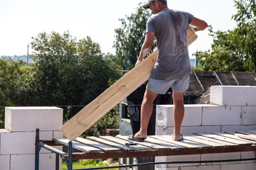 Worker builder puts a wooden beam on a brick of foam concrete
