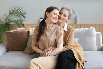 Obraz premium Portrait of old mother and mature daughter hugging at home. Happy senior mom and adult daughter embracing with love on sofa.