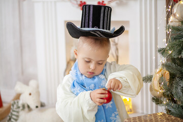 A boy with Down syndrome decorates a Christmas tree with balls, a child with a disability in a...