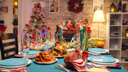 Christmas table decoration with burning candles and traditional food. Xmas celebration in decorated room full of globe decorations and christmas tree with fireplace, big festive dinner meal for large
