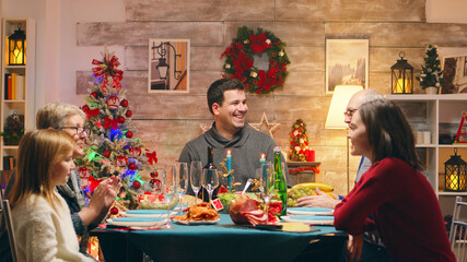 Woman arriving with chicken from the oven for christmas celebration with the family. Traditional festive christmas dinner in multigenerational family. Enjoying xmas meal feast in decorated room. Big