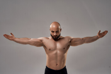 Showing his perfect body. Muscular strong bald man with naked torso standing with outstretched arms...