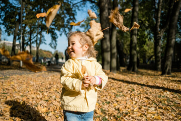 Little girl walks in the park in autumn and throws leaves