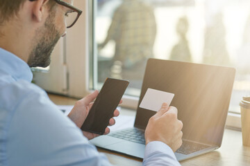 Important call. Rear view of a young businessman or male freelancer holding smartphone and looking at blank business card while working remotely in cafe