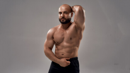 Fototapeta na wymiar Pumping up muscles. Strong athletic caucasian man bodybuilder showing his perfect body and looking at camera while posing shirtless isolated over grey background
