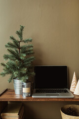 Blank screen laptop with mockup copy space on wooden stand decorated with fir tree, books, straw basket. Minimalist home office desk workspace.