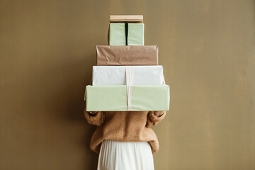 Young beautiful woman hold paper gift boxes stack against olive wall. Festive Christmas / New Year...