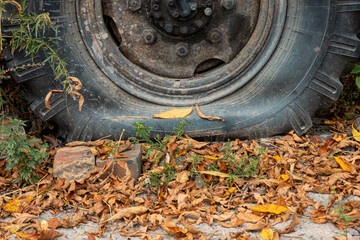 An old flat truck wheel stands on the ground covered with fallen leaves. The rubber is cracked, rust is visible on the metal part. Background. Texture.