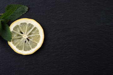 Top view of sliced yellow lemon with leaves of fresh lemon balm (Melissa officinalis) on black...