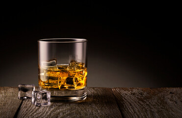 Glass of whiskey with ice cubes on wooden table.