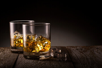 Two glasses of whiskey with ice cubes on wooden table.