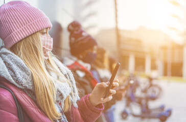 Blonde girl with face mask during coronavirus outbreak chatting on smartphone