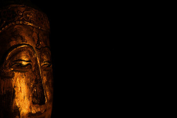 Fototapeta na wymiar Closeup of isolated illuminated golden Buddha face mask on black blank background with copy space for text