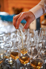 Tasting cognac or brandy. Glasses with brandy or cognac stand in a row. The waiter pours cognac into glasses, close-up