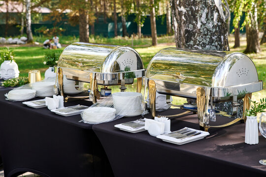 Outdoor catering banquet in summer. Banquet table with chafing dish, plates and cutlery