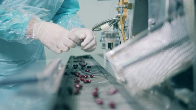 Medical worker examining pills from the conveyor