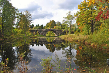Fototapeta premium Autumn day in the old park. Pond and old stone bridge
