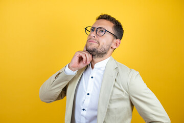 Young handsome businessman wearing suit over isolated yellow background thinking and looking to the...