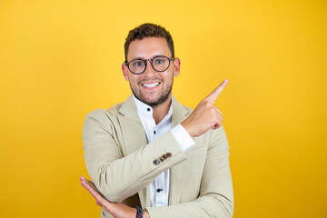 Young handsome businessman wearing suit over isolated yellow background smiling and pointing to the side with finger side.