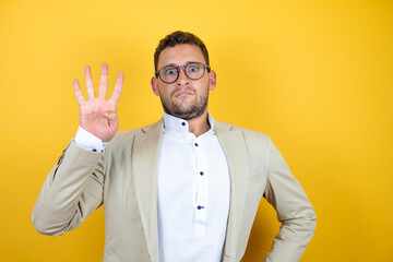 Young handsome businessman wearing suit over isolated yellow background showing and pointing up with fingers number four while smiling confident and happy