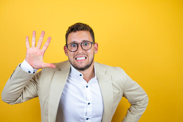 Young handsome businessman wearing suit over isolated yellow background showing and pointing up...