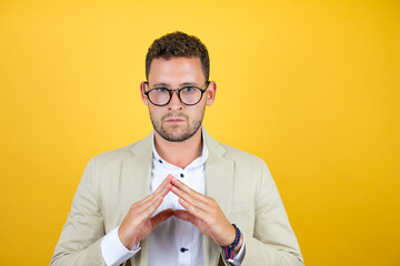 Young handsome businessman wearing suit over isolated yellow background with Hands together and...
