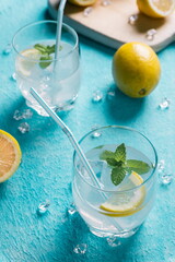 Glass of lemonade next to lemons, blue background