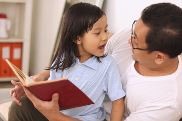 Obraz premium Happy Asian father reading book with his baby girl daughter, family enjoys quality time