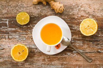 Tea of sea-buckthorn berries with lemon and ginger root on wooden background