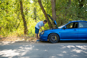 young man standing near the car with opened hood and fix some problems with engine