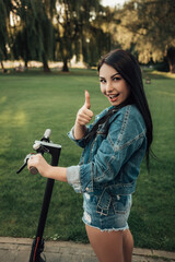 Portrait of woman with electric kick scooter standing on city street raise thumb finger up advising. Self-service street transport rental service. Rent urban eco friendly energy vehicle transportation