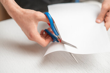 person's hands holding piece of paper sheet and cut it with scissors