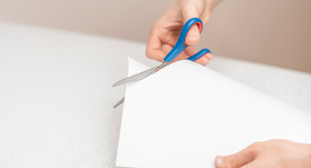 person's hands holding piece of paper sheet and cut it with scissors