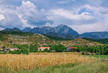 Summer landscape – valley and village in Albanian mountains, agricultural fields and gray clouds on the sky.