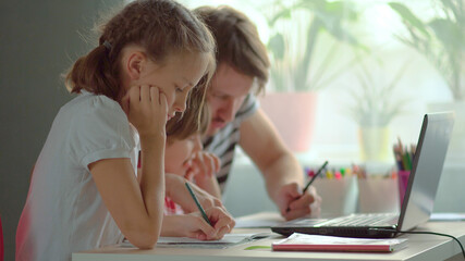 Cute children use laptop for education, online study, home studying, Boy and Girl have homework at distance learning. Lifestyle concept for home schooling. Father helps daughter and son.