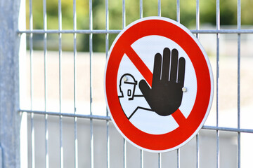 Round 'Keep out' warning sign with person holding up hand in red circle at fence protecting...