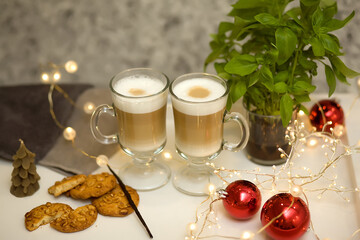 Hot chocolate cappuccino latte coffee with froth in a glass cup mug with cookies. White tray with hot drinks, garland, bokeh.