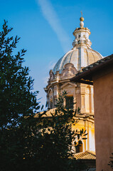 Rome, Italy - A vertical shot of the Basilica Aemilia partially covered by tree leaves during a clear sky afternoon.