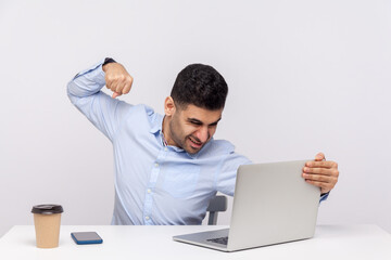 Angry businessman punching laptop screen, looking with furious mad expression, boxing threatening to hit while having online conversation, video call. indoor studio shot isolated on white background