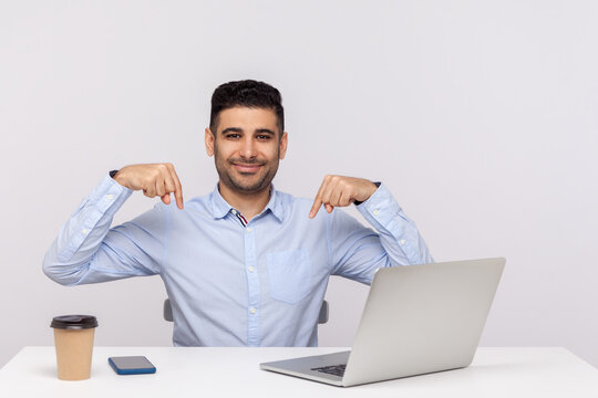 Look, advertise below! Happy elegant businessman sitting office workplace with laptop on desk, pointing down, showing place for commercial idea. indoor studio shot isolated on white background