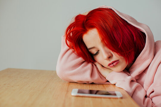 Portrait of a teen girl bored lying on desk waiting for text message on cell phone device