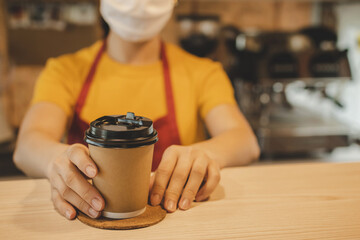 Fototapeta na wymiar friendly woman barista or waitress wearing protection face mask waiting for serving hot coffee cup to customer in cafe coffee shop, cafe restaurant, service mind, new normal, food and drink concept